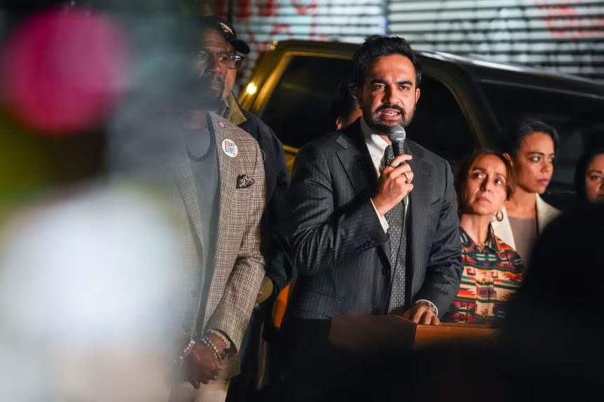 Mayor speaking into a microphone at a late-night press conference near the Bronx shooting scene, surrounded by officials and supporters